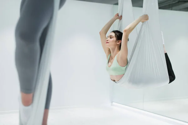 Brünette Frau hält Fliege Yoga-Hängematte während des Trainings im Sportzentrum — Stockfoto