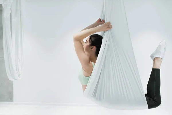 Side view of sportswoman exercising on fly yoga hammock in fitness center — Stock Photo