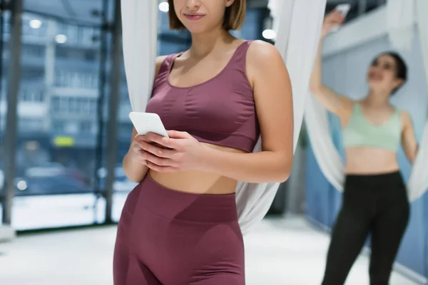 Ausgeschnittene Ansicht einer jungen Frau mit Smartphone in der Nähe der Hängematte von Fliegenyoga — Stockfoto