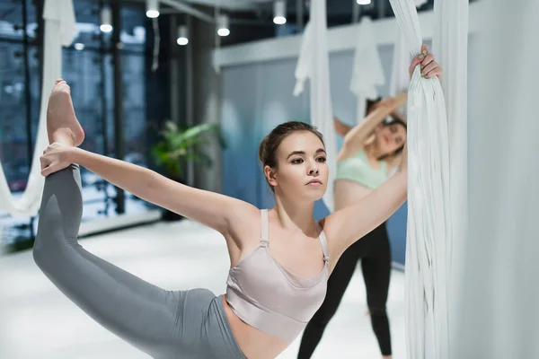Jeune femme étirant la jambe pendant la formation de yoga de mouche — Photo de stock