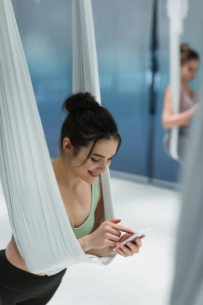 Fröhliche Frau benutzt Handy beim Fliegenyoga-Training — Stockfoto