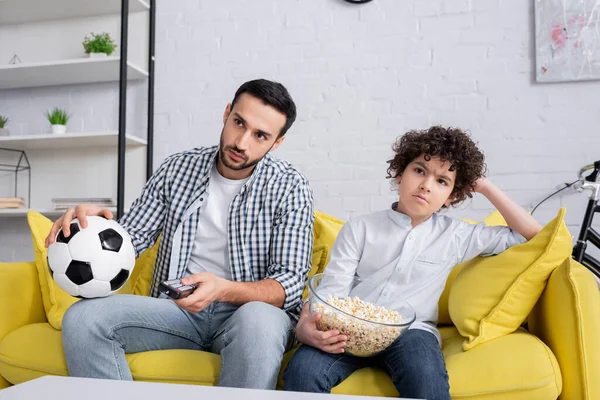 Molesto papá musulmán e hijo viendo campeonato de fútbol en la televisión en casa - foto de stock