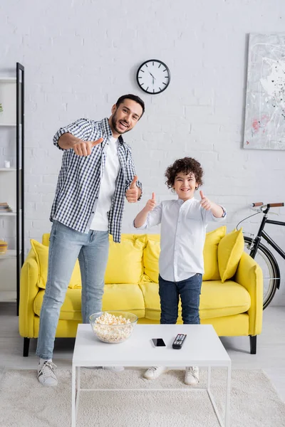 Emocionado musulmán padre e hijo mostrando los pulgares hacia arriba mientras mira a la cámara - foto de stock