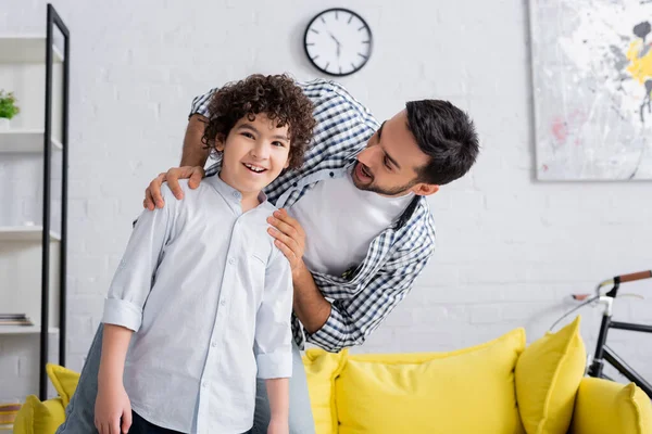 Young muslim man embracing shoulders of son smiling at camera at home — Stock Photo