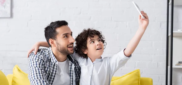 Happy arabian boy taking selfie on mobile phone together with father, banner — Stock Photo