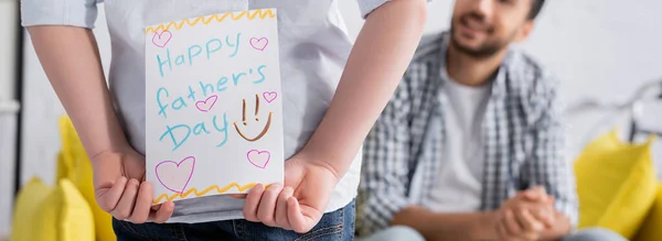 Cropped view of kid holding happy fathers day card near muslim dad on blurred background, banner — Stock Photo