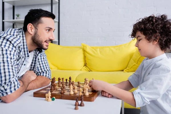 Smiling muslim man looking at son playing chess at home — Stock Photo