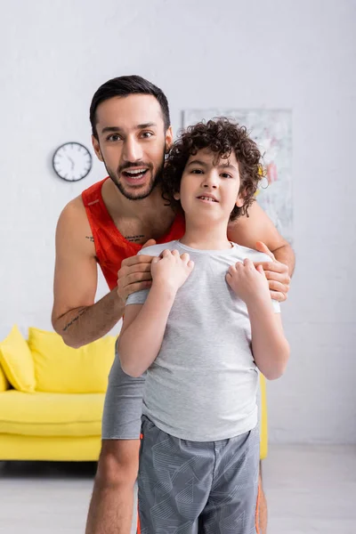 Улыбающийся мусульманский отец обнимает сына в спортивной одежде дома — Stock Photo