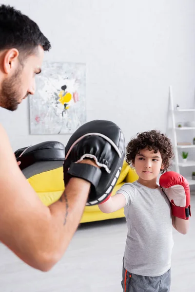 Niño musulmán en guantes de boxeo boxeo con padre en guantes de ponche en primer plano borroso - foto de stock