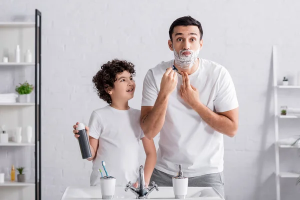 Arabian man shaving beard near smiling son with foam in bathroom — Stock Photo