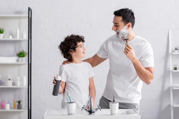 Happy muslim man shaving beard and hugging son with foam in bathroom — Stock Photo