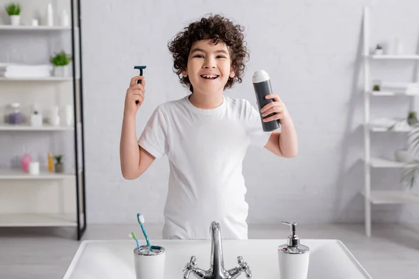 Улыбающийся арабский мальчик с бритвой и пеной для бритья в ванной — стоковое фото