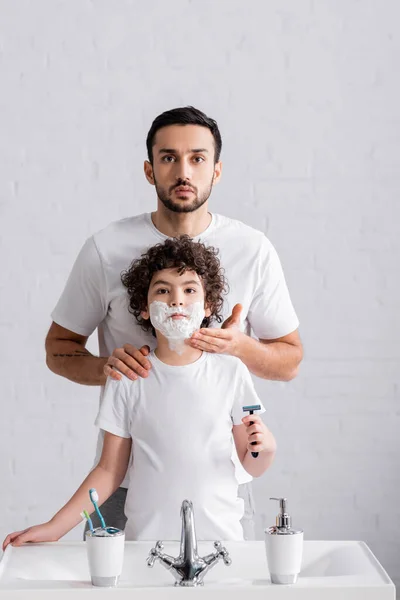Muslim man applying shaving foam on face of son with razor — Stock Photo