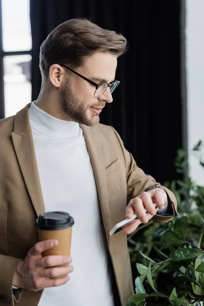 Young businessman looking at wristwatch while holding coffee to go in office — Stock Photo