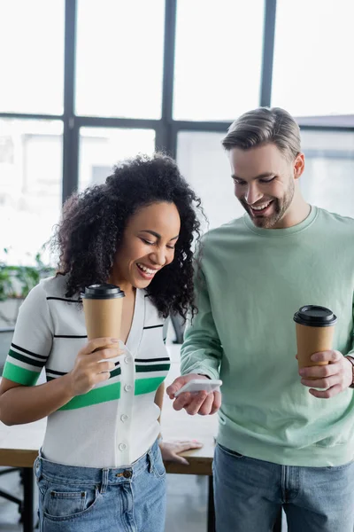 Smiling businessman showing mobile phone to cheerful african american colleague — Stock Photo
