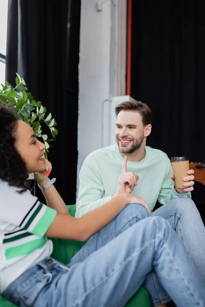 Улыбающийся бизнесмен показывает пальцем, разговаривая с африканским американским коллегой на размытом переднем плане — стоковое фото