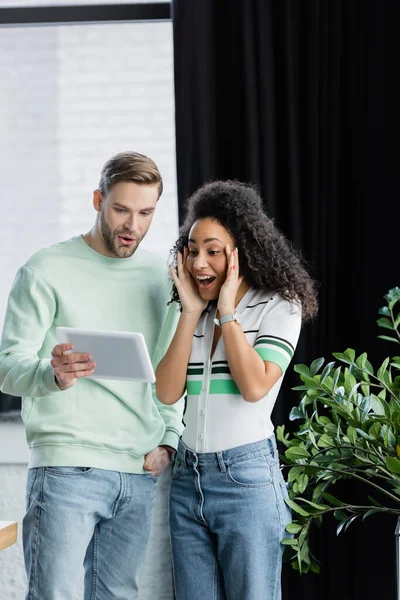Astonished african american businesswoman looking at digital tablet in hands of amazed colleague — Stock Photo
