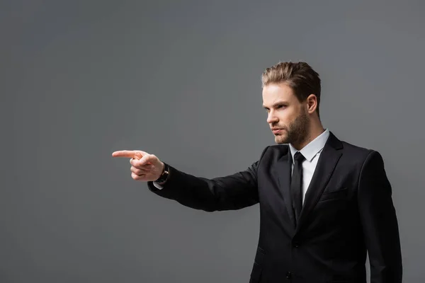 Serious businessman looking away and pointing with finger isolated on grey — Stock Photo