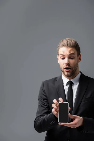 Surprised businessman holding mobile phone with blank screen isolated on grey — Stock Photo