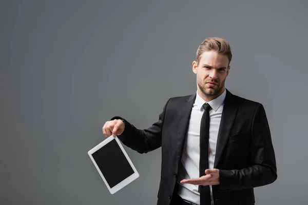 Displeased businessman pointing at broken digital tablet with blank screen isolated on grey — Stock Photo