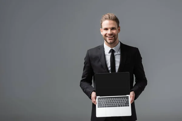 Joyful manager showing laptop with blank screen isolated on grey — Stock Photo