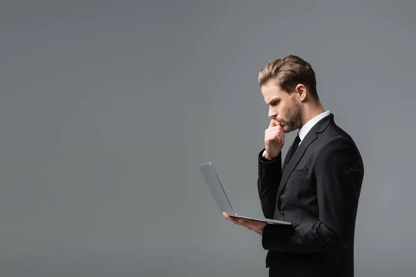 Side view of thoughtful businessman looking at laptop isolated on grey — Stock Photo