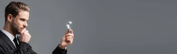 Thoughtful businessman looking at light bulb isolated on grey, banner — Stock Photo