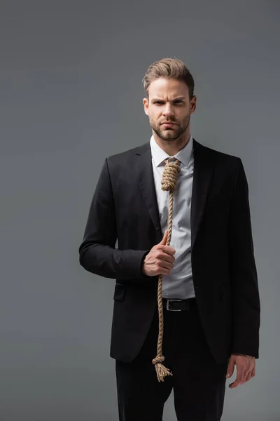 Empresário tenso em terno preto, com corda em vez de gravata, olhando para câmera isolada em cinza — Fotografia de Stock