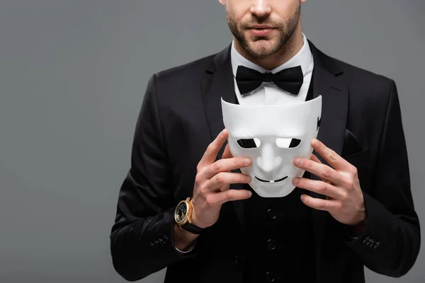 Обрізаний вид бізнесмена в чорному костюмі, що тримає маску для обличчя ізольовано на сірому — стокове фото