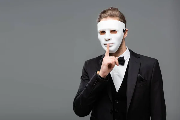 Young businessman in face mask showing secret gesture isolated on grey — Stock Photo