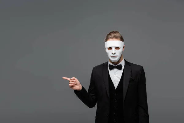 Elegante hombre de negocios en mascarilla apuntando con el dedo aislado en gris - foto de stock