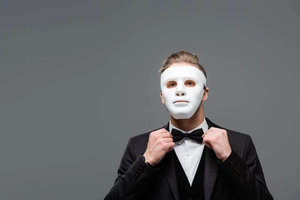 Elegant businessman in face mask adjusting bow tie isolated on grey — Stock Photo