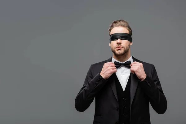 Elegant, blindfolded businessman adjusting bow tie isolated on grey — Stock Photo