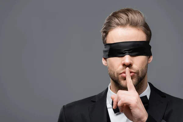 Homme d'affaires dans les yeux bandeau montrant signe de silence isolé sur gris — Photo de stock