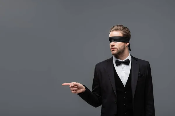 Blindfolded businessman in black suit pointing away with finger isolated on grey — Stock Photo