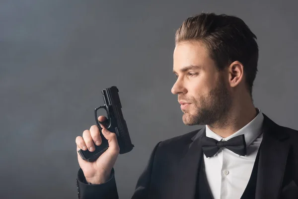 Young, confident businessman holding weapon on grey background with smoke — Stock Photo