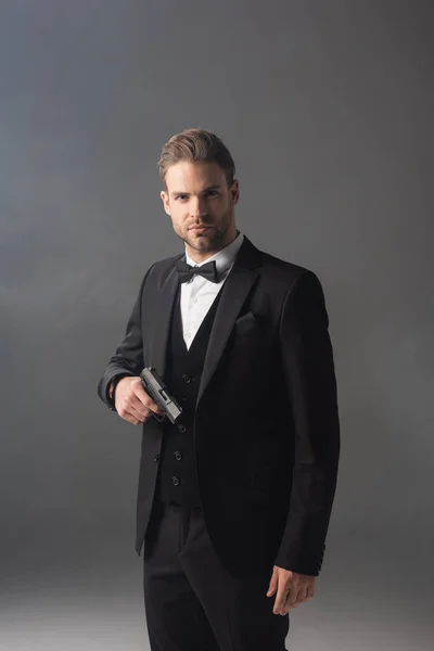 Confident businessman looking at camera while standing with gun on grey background with smoke — Stock Photo