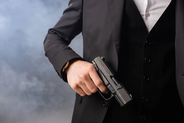 Частичный взгляд бизнесмена с пистолетом на сером фоне с дымом — стоковое фото