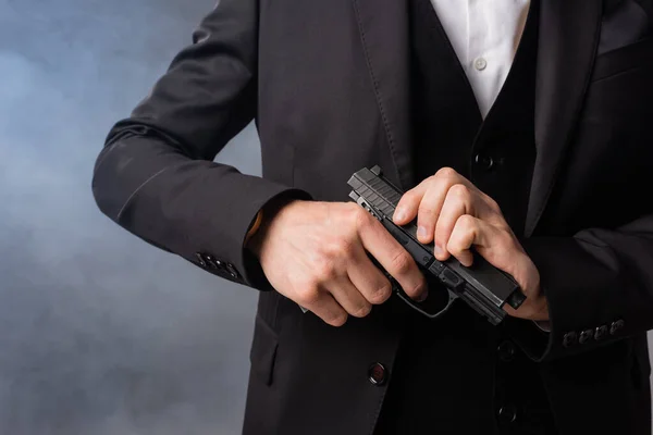 Vista parcial del empresario armado en traje negro sobre fondo gris con humo - foto de stock