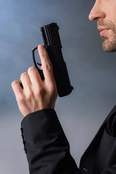 Обрезанный вид бизнесмена с пистолетом на сером фоне с дымом — стоковое фото