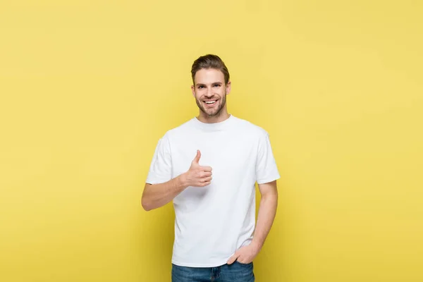 Smiling man with hand in pocket showing like on yellow — Stock Photo