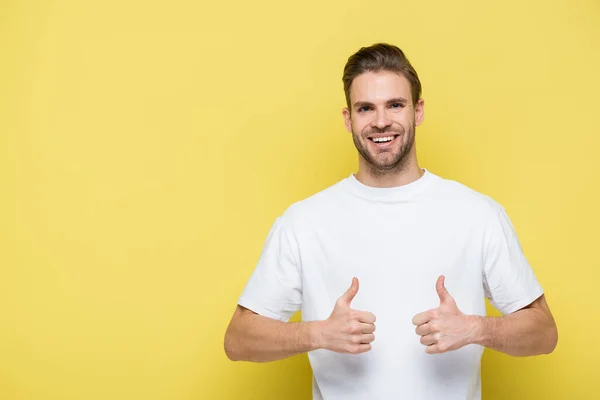 Complacido hombre sonriendo a la cámara y mostrando los pulgares hacia arriba en amarillo - foto de stock