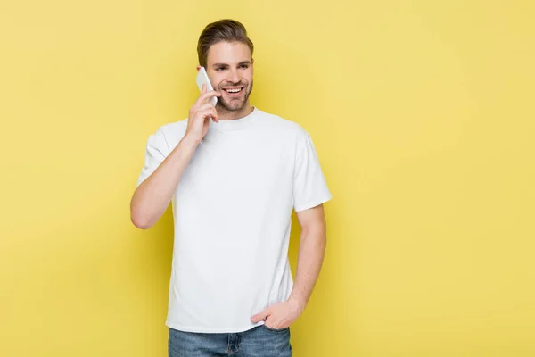 Smiling man holding hand in pocket during conversation on mobile phone on yellow — Stock Photo