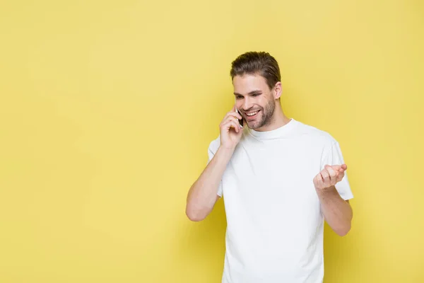Homem feliz apontando com o dedo enquanto fala no smartphone no amarelo — Fotografia de Stock
