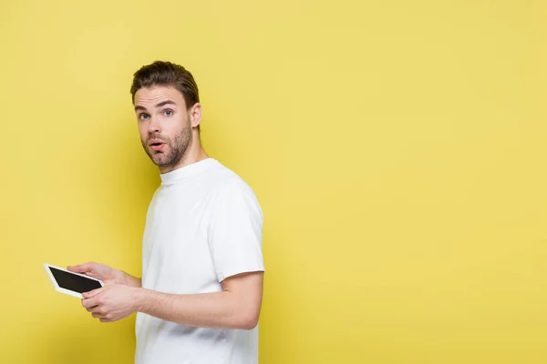 Обескураженный мужчина смотрит в камеру, стоя с цифровым планшетом на желтом — стоковое фото