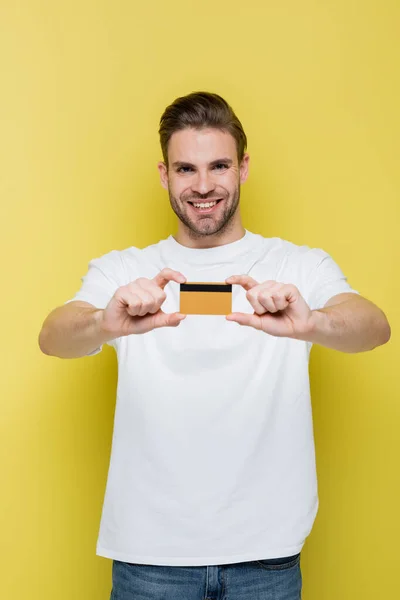 Задоволений чоловік показує кредитну картку, посміхаючись на камеру жовтого кольору — стокове фото