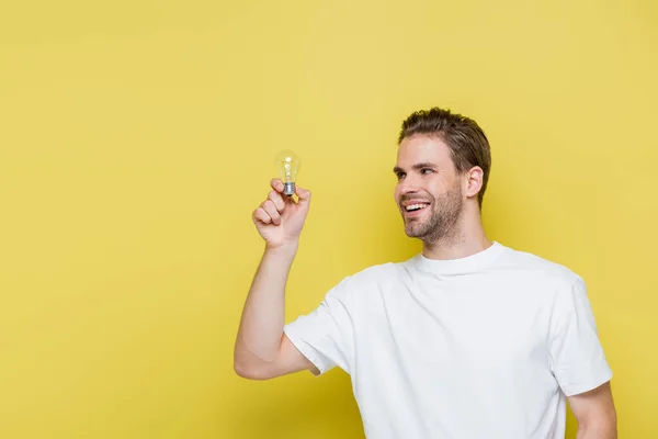 Homme joyeux regardant ampoule sur jaune — Photo de stock