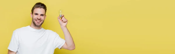 Pleased man looking at camera while holding light bulb on yellow, banner — Stock Photo