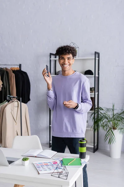 Souriant propriétaire afro-américain de showroom tenant smartphone près de la table de travail — Photo de stock