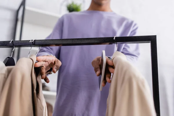 Cropped view of african american small business owner holding cellphone near jackets on blurred foreground — Stock Photo